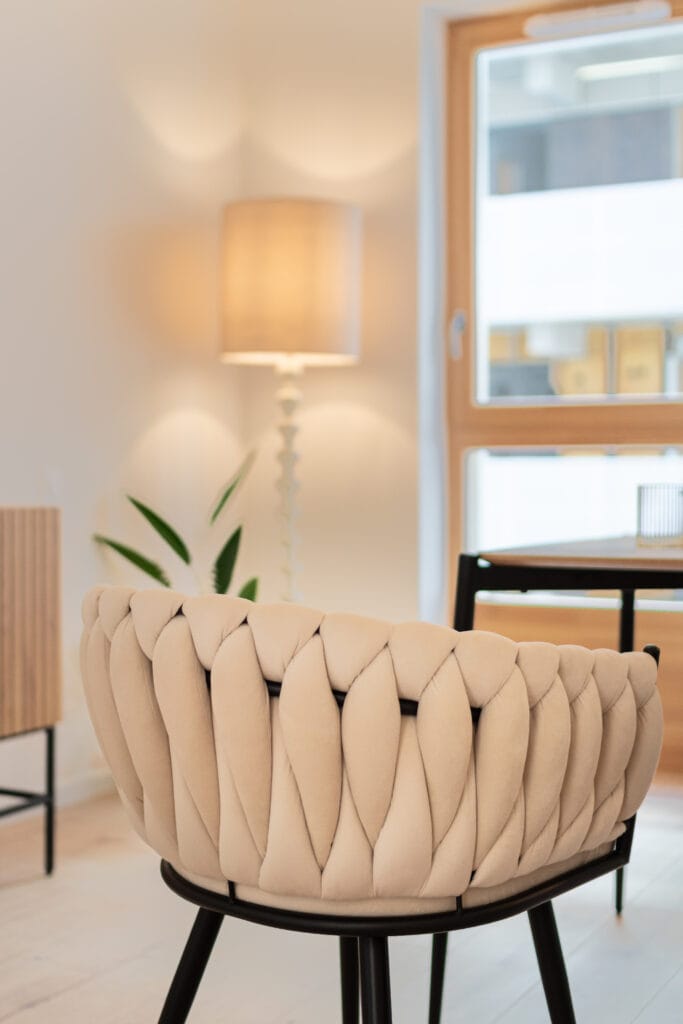 Fauteuil beige dans un intérieur d’appartement à Nancy, avec lampe, plante et fenêtre en bois