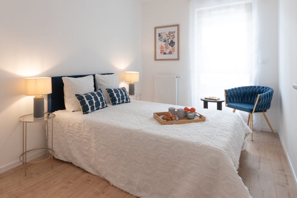 Chambre parentale d’un appartement à Nancy avec lit double, fauteuil bleu et lumière naturelle